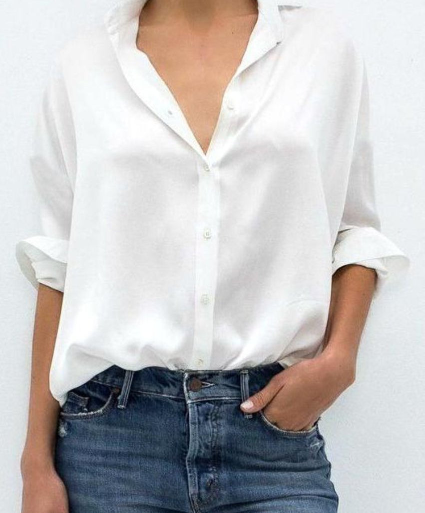 Simple mid body shot of a woman wearing a white oxford shirt tucked into jeans. One of her hands is in her pocket.