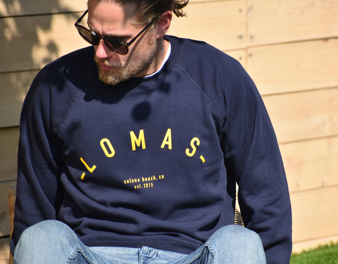 Man who is wearing Navy Crewneck Sweatshirt with yellow/gold lettering that says "Lomas, Solana Beach, CA, EST 2015" - The Lomas Brand