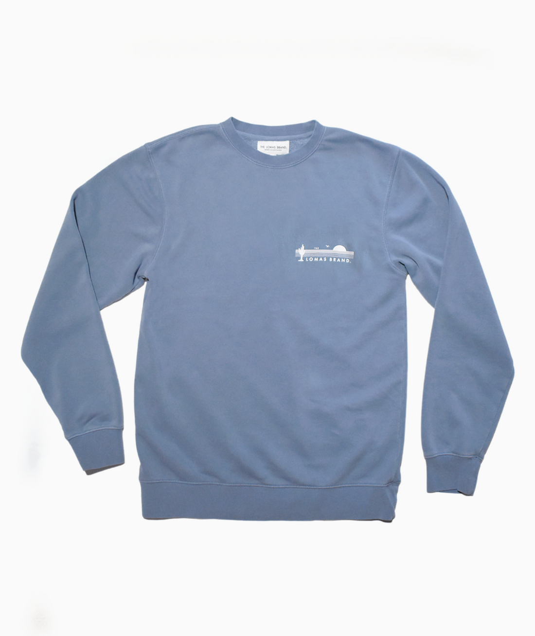 Cozy and warm faded blue crewneck sweatshirt. The upper left of the sweatshirt features The Lomas Brand saguaro logo in white. The logo has a saguaro cactus, bird, and a rising sun in white. 'The' is printed above the logo and 'Lomas Brand' is printed below.