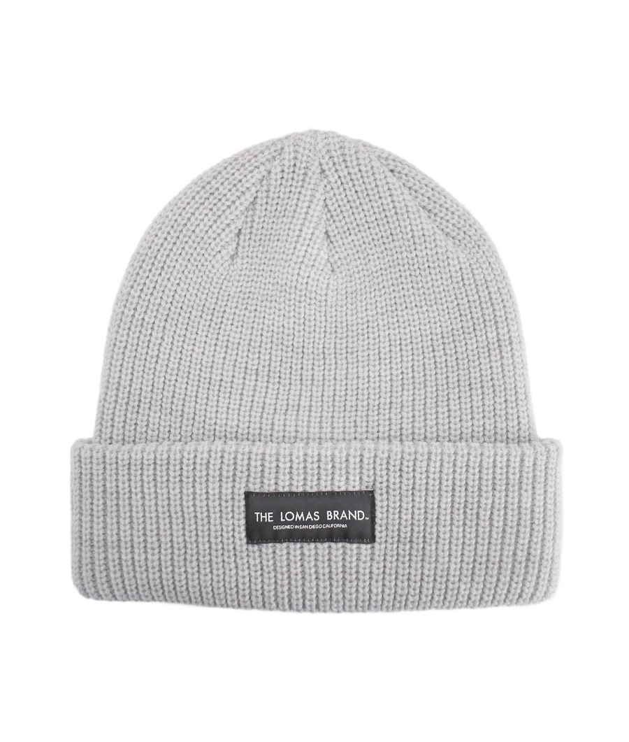 Plush, comfortable, and warm grey beanie with a black patch sewn on the front. The patch has 'The Lomas Brand' in white with 'Designed in San Diego California' below. 