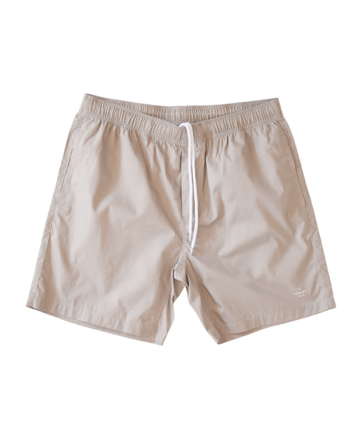 Mens premium taupe swim trunk board shorts. The inside front of the shorts have a white drawstring and the lower left leg features a small The Lomas Brand circular logo in white. 