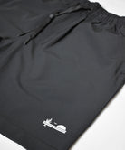 Mens premium black thick, stretchy, and versatile shorts with a drawstring. The photo features a close up of the lower left side of the shorts with The Lomas Brand logo in white. The logo has a saguaro cactus, bird, and a rising sun.