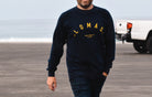 Man wearing a navy blue sweatshirt, standing on a beach. The ocean and a white vehicle are visible in the background. The sweatshirt text includes "LOMAS" written in an arch, and "est. 2015" beneath "solana beach, ca," all in yellow.