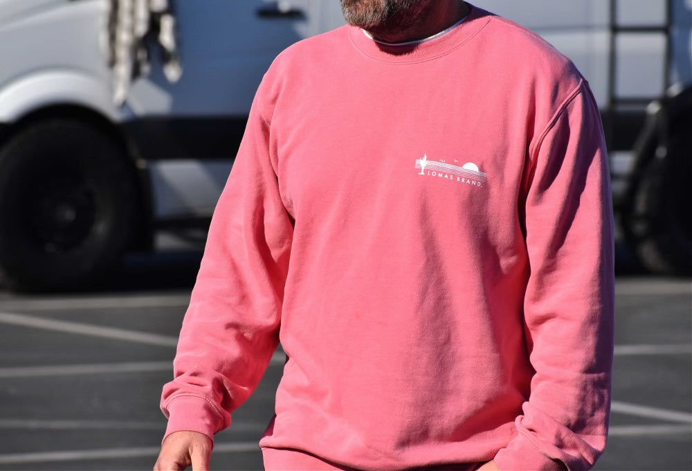 Man wearing a salmon colored sweatshirt with a small white graphic on the chest. Only the torso is visible. There's a vehicle in the background, suggesting this is in a parking lot or street setting.