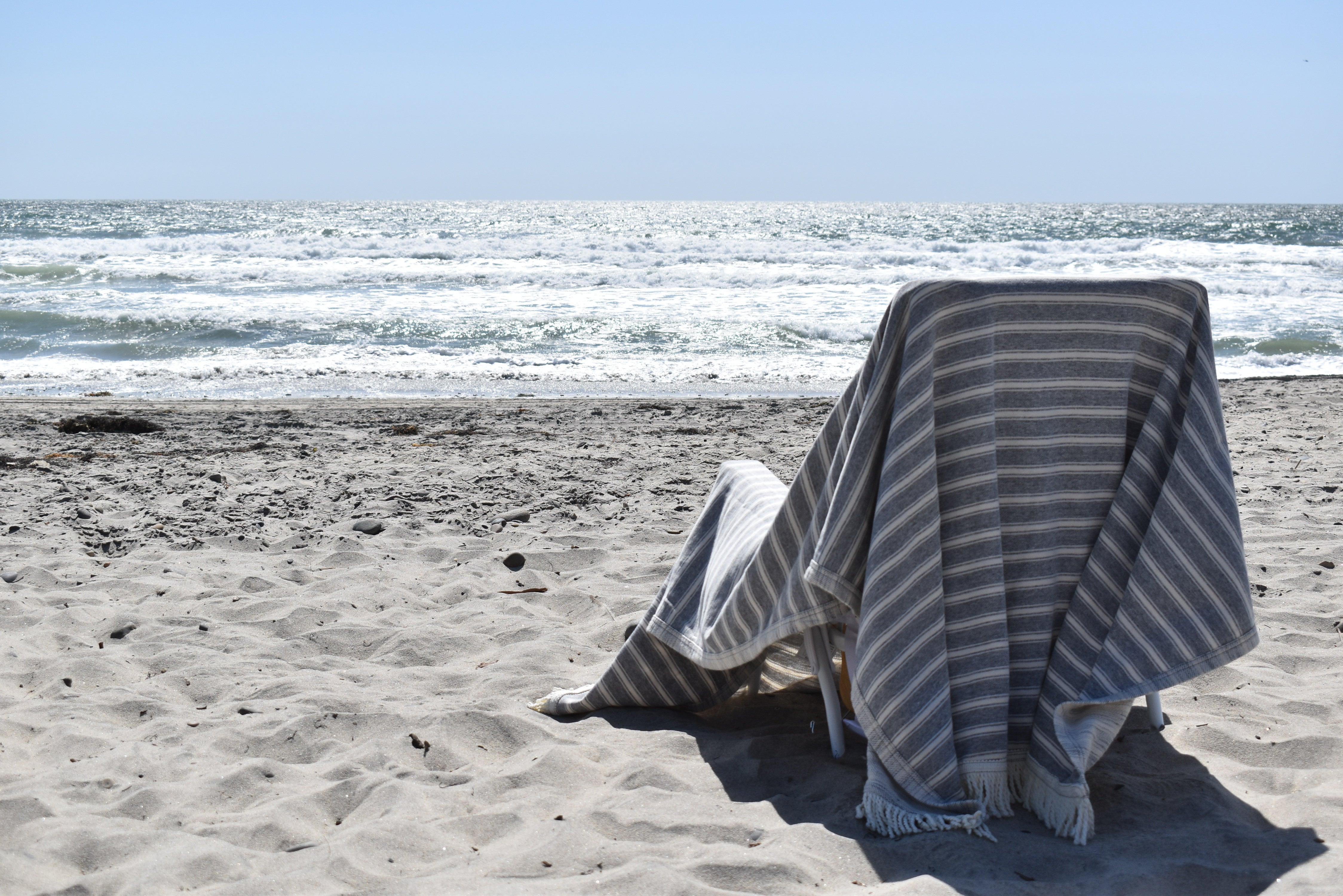 Grey and white striped beach blanket displayed over a chair on the beach facing the ocean.