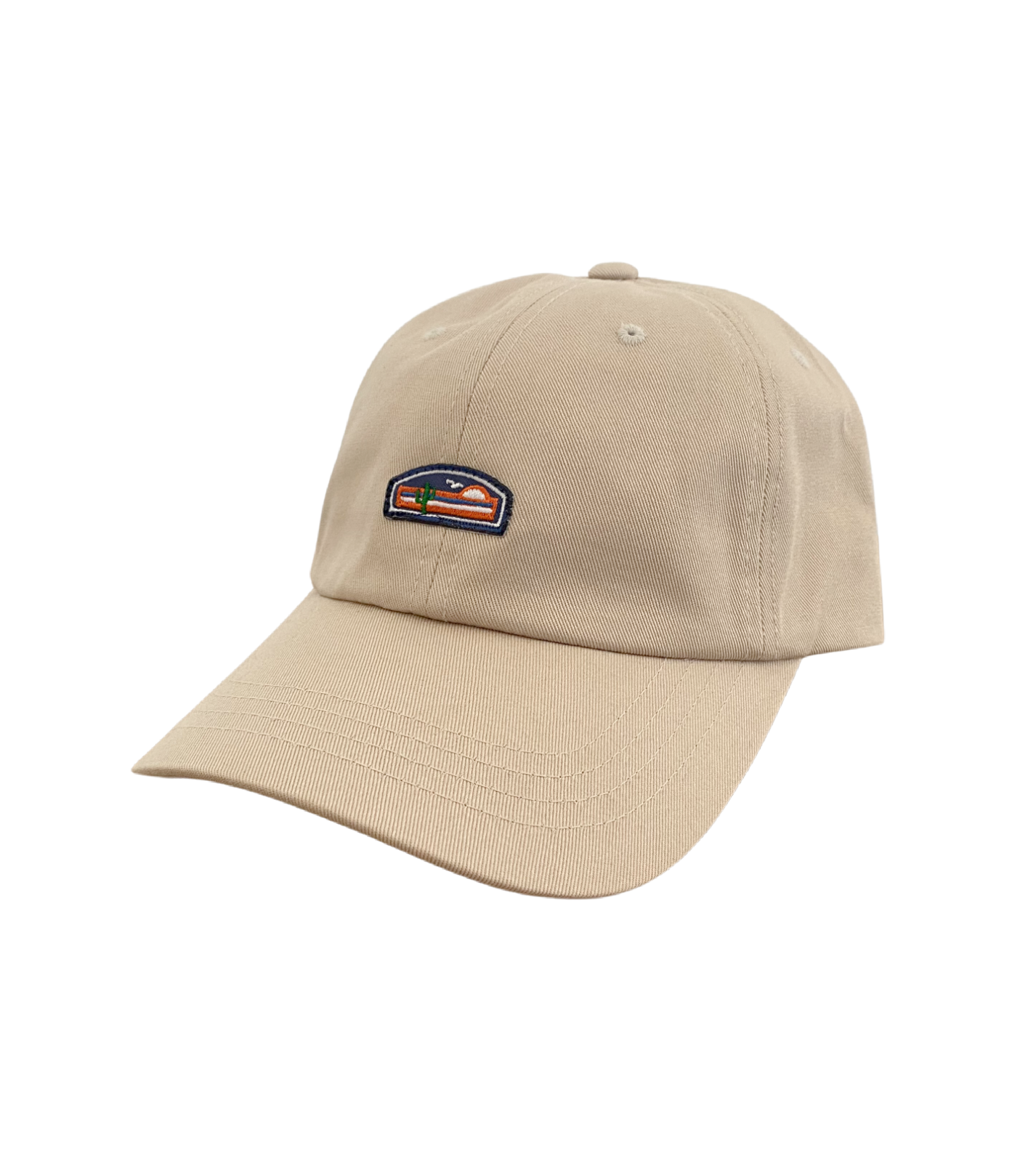 Tan baseball cap with a small embroidered logo on the front. The logo features a sun, mountains, and cactus design. The cap is photographed at an angle against a white background.