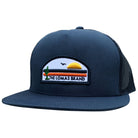 A navy blue trucker-style hat with a patch on the front. The patch has a desert scene with a cactus, sun, and "THE LOMAS BRAND" text.