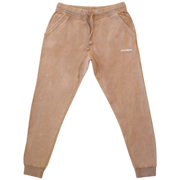 Tan-colored joggers laid flat. The pants have an elastic waistband with a drawstring, side pockets, and tapered legs with elastic cuffs at the ankles. The 