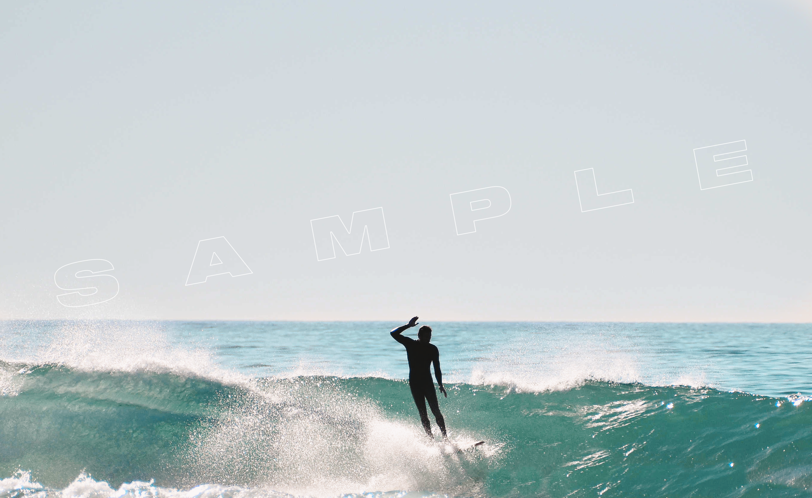 A silhouette of a surfer riding a large wave, with water spraying behind them. The ocean and sky are visible in the background. The word "SAMPLE" is overlaid on the image.