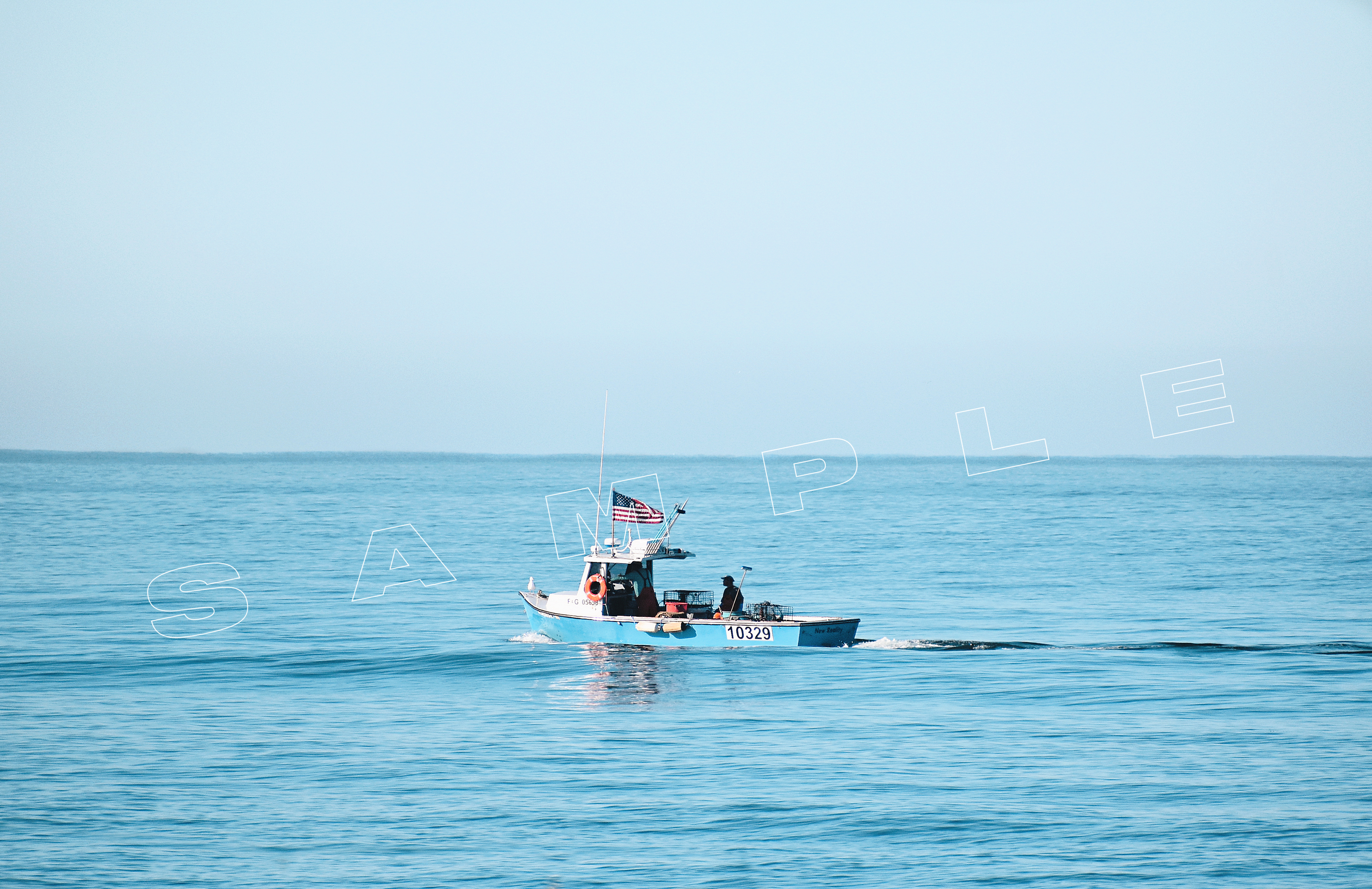 A small blue fishing boat with the number 10329 visible on its side is sailing on calm blue waters. The boat is flying an American flag and appears to have one person on board. The sky is clear and light blue, blending with the horizon. In the foreground of the image, the word "SAMPLE" is partially visible, overlaid in white text.